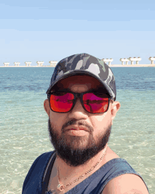 a man with a beard wearing sunglasses and a hat stands in the water