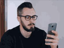 a man wearing glasses looks at a cell phone