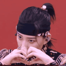 a woman wearing a headband and earrings makes a heart with her hands