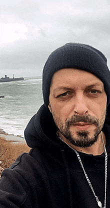 a man with a beard wearing a black beanie and a necklace