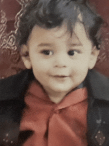 a young boy wearing a red bow tie and a black jacket looks at the camera