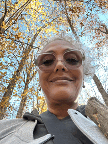 a woman wearing sunglasses is smiling in front of a tree