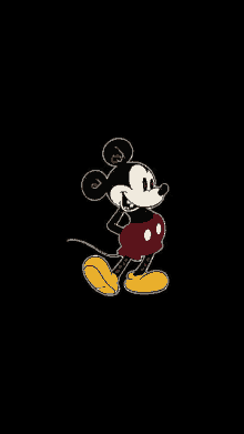 mickey mouse is standing on a black background and looking at the camera .