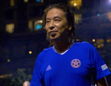 a man wearing a blue adidas shirt stands in front of a building