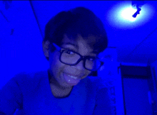 a boy wearing glasses and a blue shirt is smiling in front of a blue light