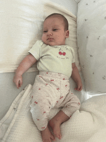 a baby wearing a green shirt with cherries on it laying on a bed