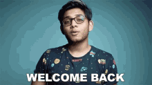 a young man wearing glasses is standing in front of a blue background and says `` welcome back '' .