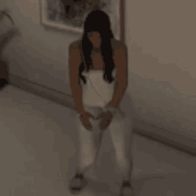 a woman in a white dress is standing in a room with her hands on her knees .