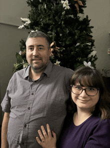 a man and woman are posing in front of a christmas tree