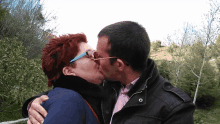 a man and a woman are kissing in front of some trees