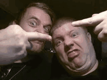 two men are making funny faces for the camera while pointing at each other with their fingers .