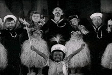 a black and white photo of a group of children dressed as sailors and hula dancers .