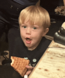 a little boy with a surprised look on his face is holding a piece of food