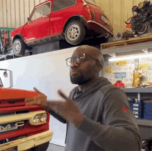 a man wearing glasses is standing in front of a red car with a license plate that says vw 3150 h6 15