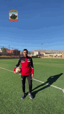 a man in a red and black jacket holds a soccer ball on a soccer field with a logo that says juventus