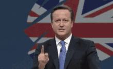 a man in a suit and tie is giving a speech in front of a flag of the united kingdom .