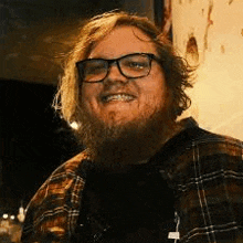 a man with a beard wearing glasses and a plaid shirt is smiling for the camera .