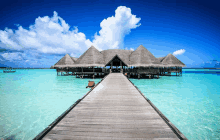 a wooden pier leading to a thatched hut in the middle of the ocean