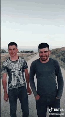 two men are standing next to each other on a dirt road holding hands .