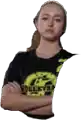 a woman is standing with her arms crossed and wearing a black t-shirt with a yellow logo on it .