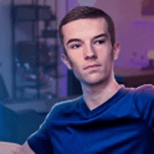 a young man in a blue shirt is sitting in a chair looking at the camera .