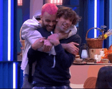 a man with pink hair is hugging another man in a kitchen