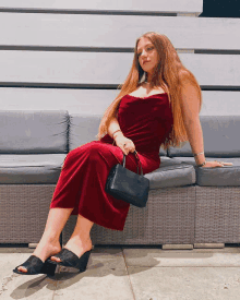 a woman in a red dress sits on a couch holding a black bag