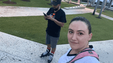 a man and a woman are rollerblading in a park and the man is looking at his phone