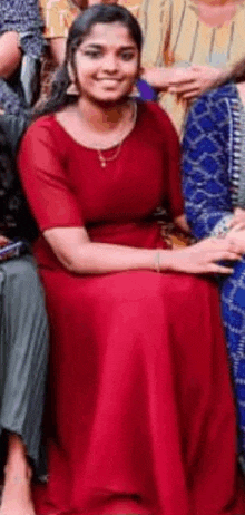 a woman in a red dress is sitting in a group of people and smiling .