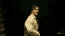 a man in a white jacket is standing in a dark room with a disney logo behind him