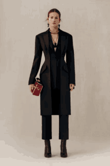 a woman in a black coat and pants is holding a red bag