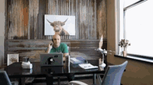 a man sits at a desk with an apple laptop and a picture of a bull on the wall behind him