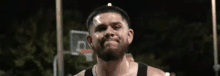 a man with a beard is standing next to a basketball hoop at night .