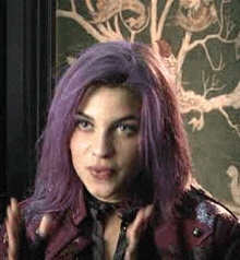 a woman with purple hair is wearing a leather jacket and gloves .