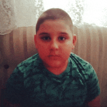 a young boy wearing a green shirt looks at the camera