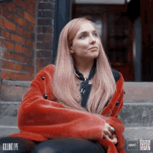 a woman in a red fur coat is sitting on a set of stairs with a bbc america logo behind her