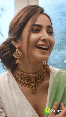 a woman wearing a gold necklace and earrings is laughing with ola party in the bottom right corner