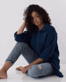 a woman sitting on the floor wearing a blue shirt and jeans