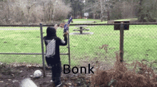 a boy holding a nerf gun in front of a chain link fence with the word bonk written on it