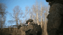 a soldier is holding a sniper rifle in a forest .