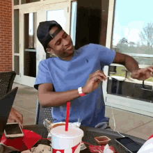 a man in a blue shirt is sitting at a table with a cup of soda and a red straw