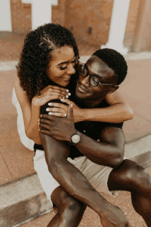 a man wearing glasses is hugging a woman who is wearing a ring on her finger