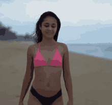 a young woman in a pink bikini is walking on the beach