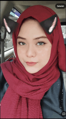 a woman wearing a red hijab and black cat ears looks at the camera