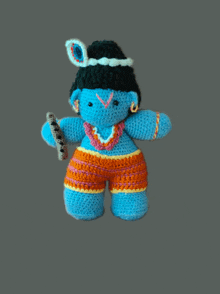 a crocheted doll of a blue elephant with a black hat and orange shorts