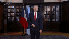 a man in a suit and tie is standing in front of a library with the word voyo on the wall