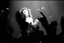 a black and white photo of a woman singing into a microphone in front of a crowd of people .