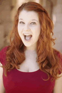 a woman with red hair and a red shirt is making a funny face with her mouth open .