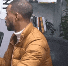 a man in a brown jacket sits in front of a bookshelf with a book called make fashion history on it