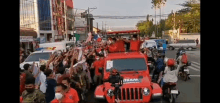 a group of people are standing around a red jeep on a city street .